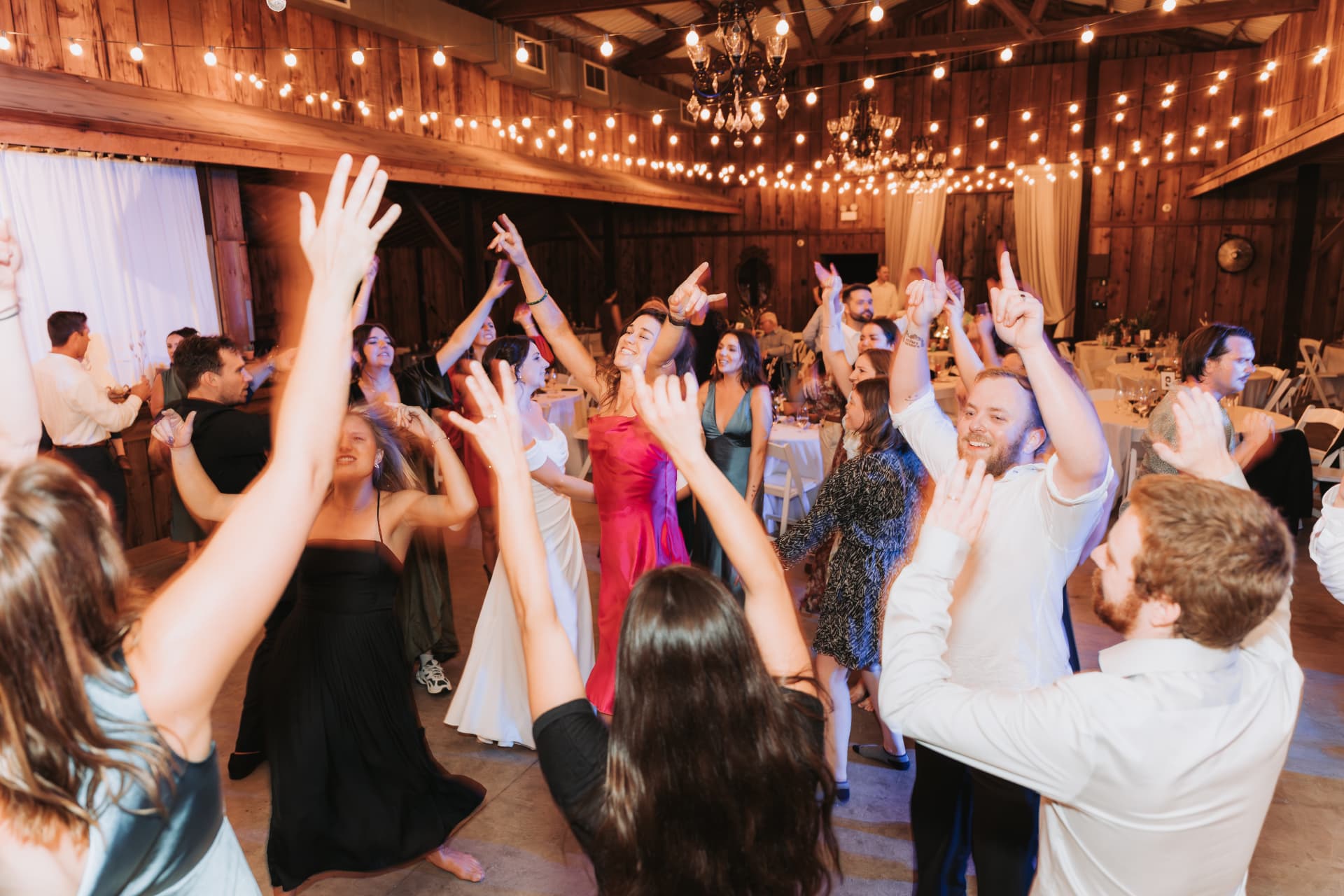 Packed dance floor under string lights at a barn wedding reception
